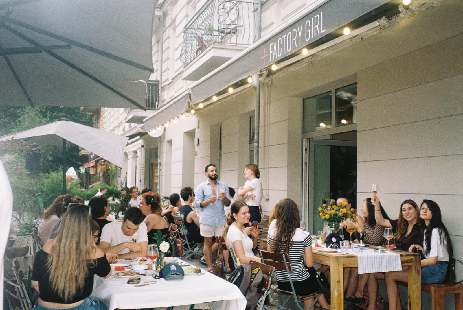 The terrace at FACTORY GIRL Berlin on a summer afternoon, with customers at tables outside and the FACTORY GIRL sign above the entrance